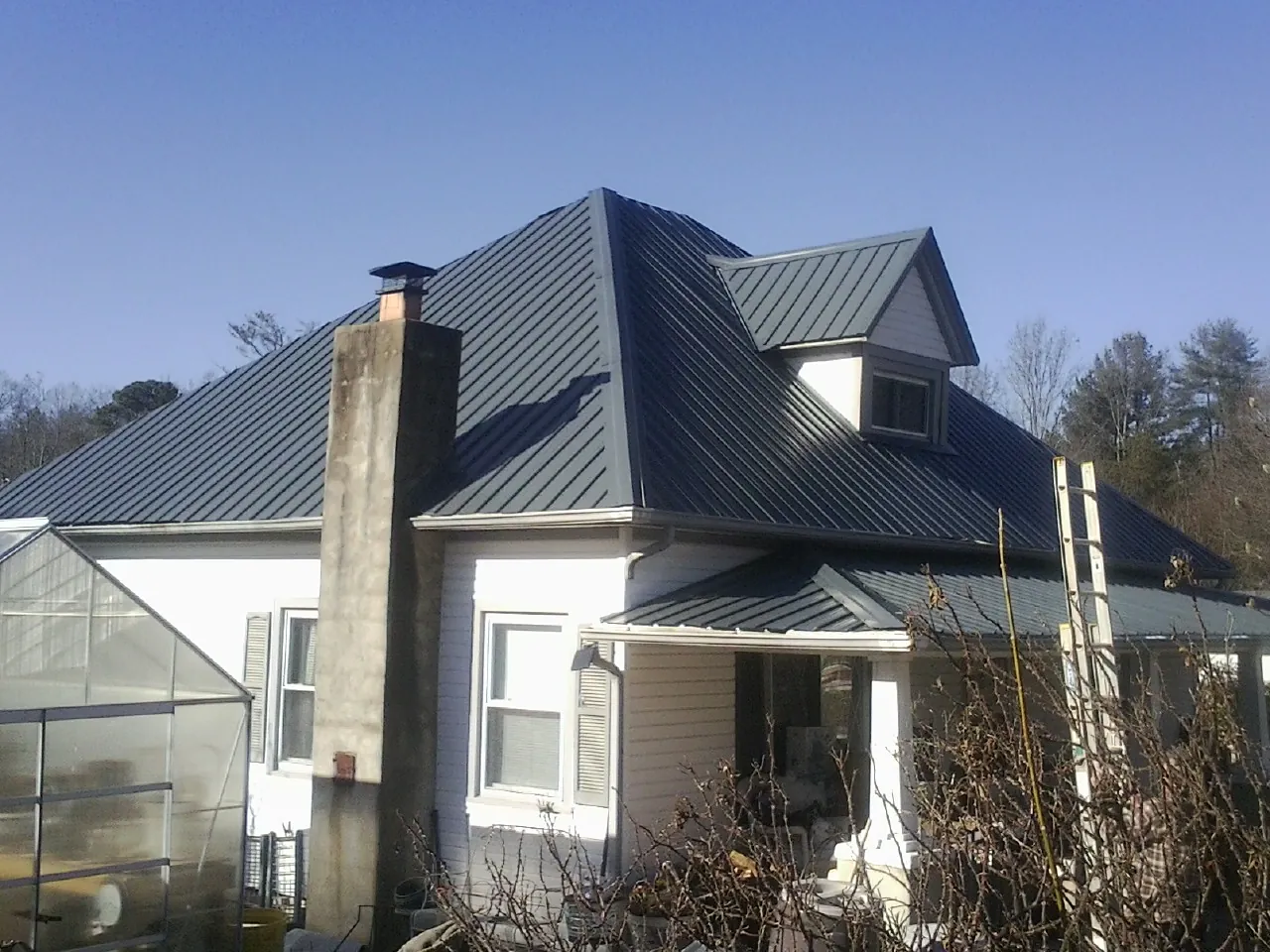 Dark blue standing seam metal roof on a white farmhouse with dormer — Slate & Tile Roof Repair by Roofing Brothers in Baytown
