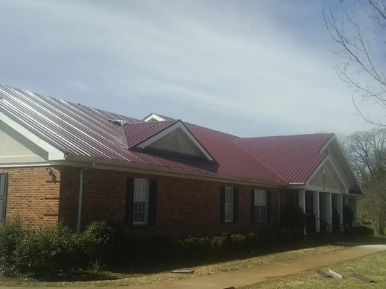 Red metal roof with gabled entries on a long brick building, from a Hail Damage Roof Repair job in Baytown