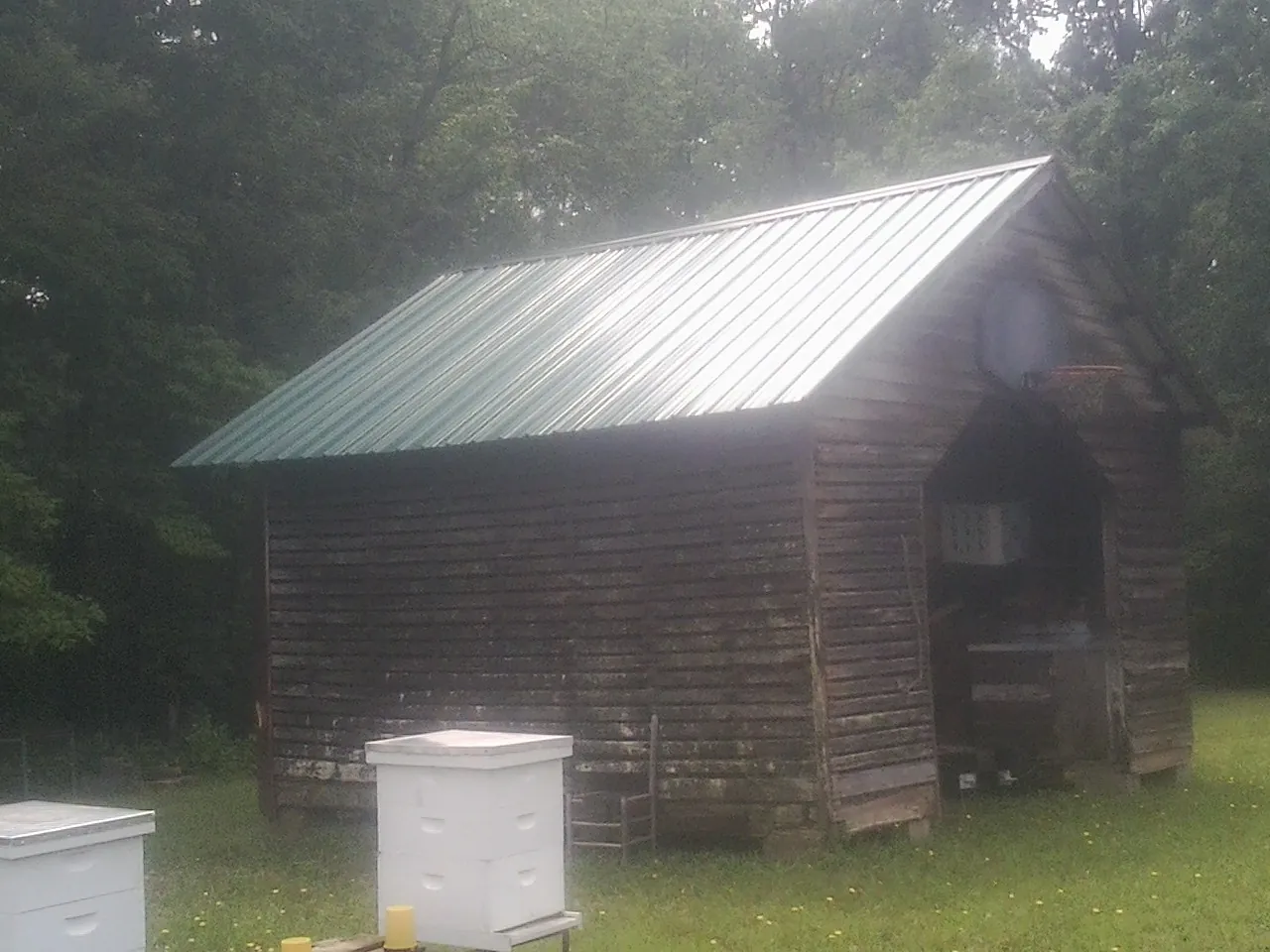 Green metal roof on a weathered barn beside stacked beehives in Baytown
