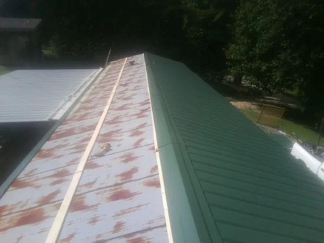 Old rusted panels beside newly installed green metal roofing — Wind Damage Roof Repair by Roofing Brothers in Baytown