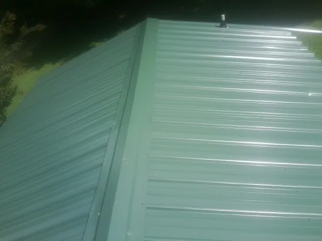 New green metal panels meeting at the ridge of a roof — Flat Roof Repair work by our crew in Baytown