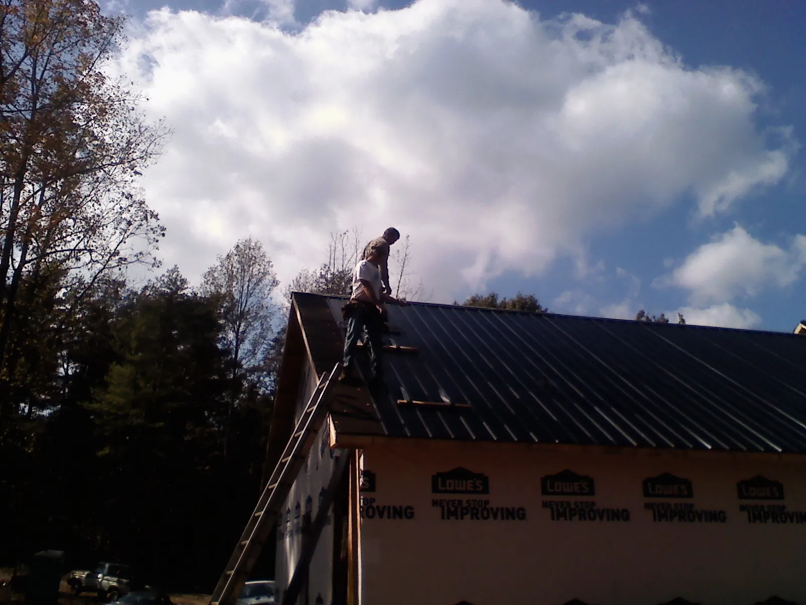 Roofer fastening dark metal panels high against a cloudy sky, from a Roof Inspection job in Baytown